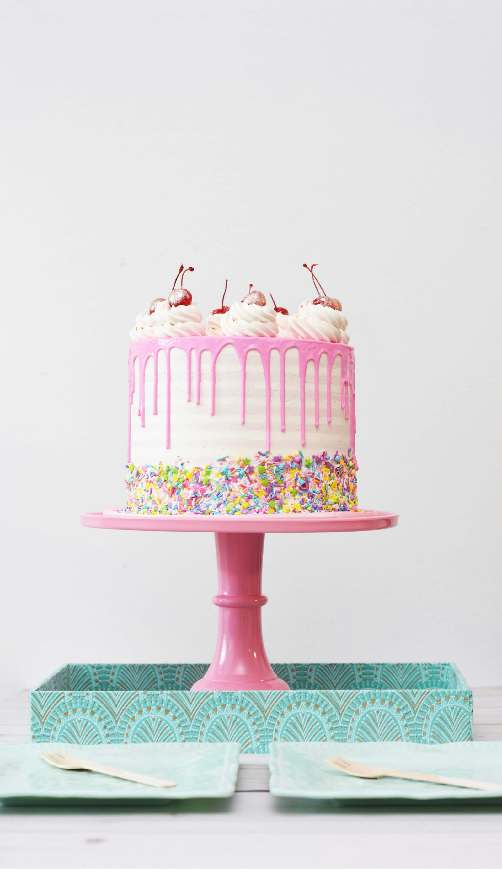 Bolo rosa com cobertura drip, confeitos coloridos e cerejas em um pedestal rosa