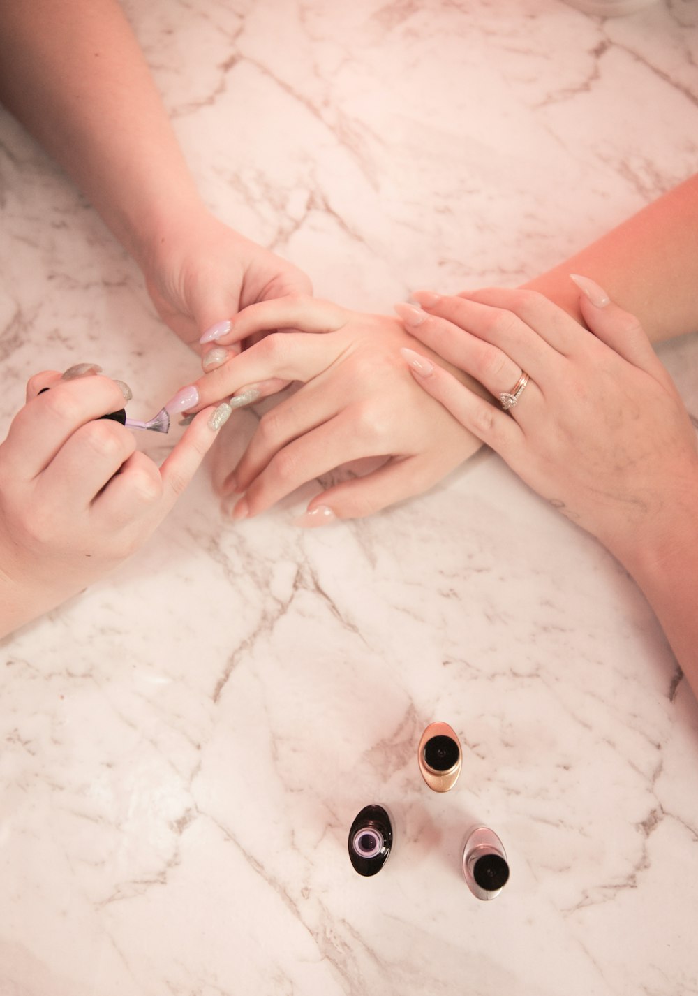 Mãos com unhas em tom suave sobre uma superfície de mármore