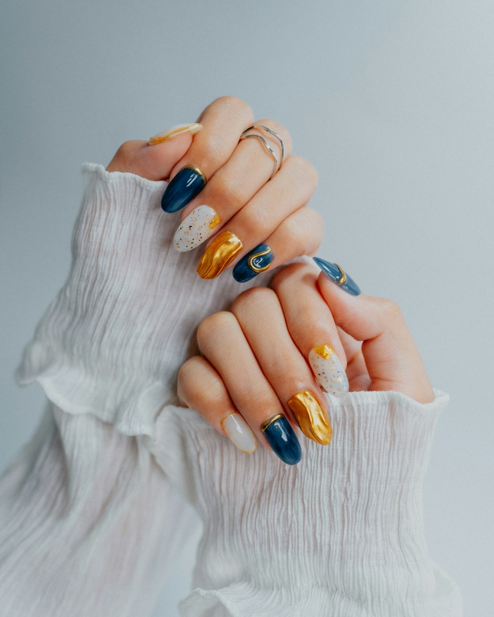 Nail art expressiva com azul profundo, dourado e detalhes artísticos
